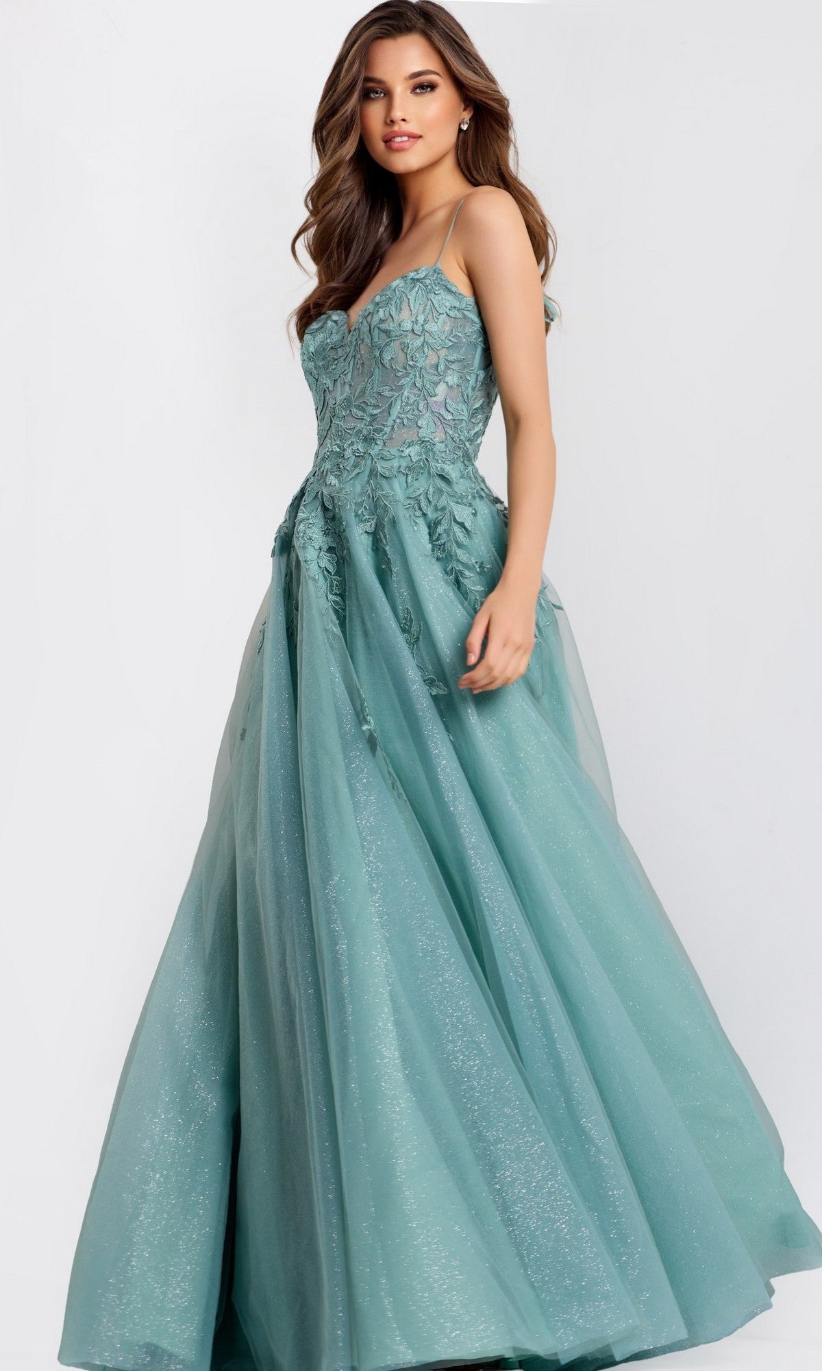 A woman wears the Jovani 49092 Long Prom Dress, a sleeveless teal gown with a fitted embroidered bodice adorned with lace appliques and a voluminous tulle skirt featuring a subtle glitter finish.